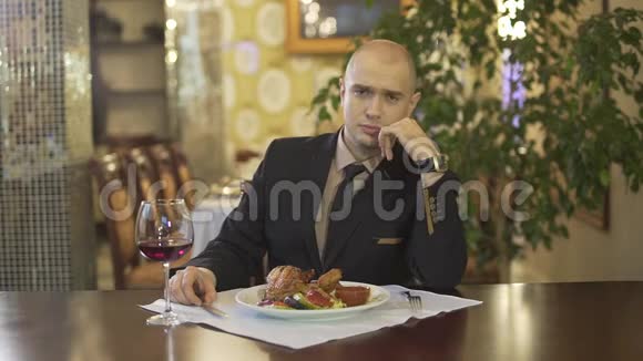 聪明迷人的光头男穿着经典西装独自一人在高级餐厅切烤鸡肉餐视频的预览图
