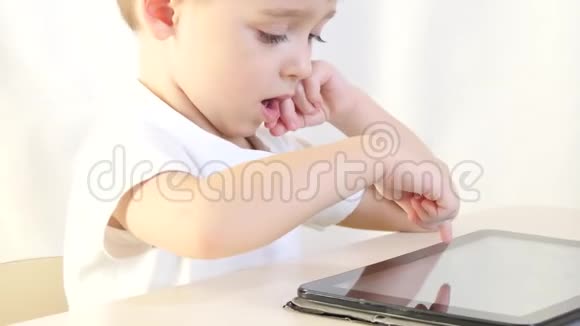 快乐的孩子坐在桌子旁玩平板电脑孩子乐于玩电子游戏儿童的概念视频的预览图