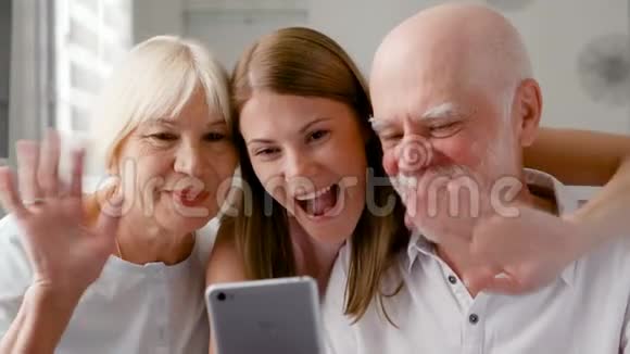 年长夫妇和他们的女儿在家里通过手机上的信使Skype聊天微笑着笑视频的预览图