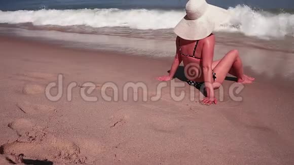穿着比基尼和白色太阳帽的女性在海沙天堂海滩上日光浴的后景视频的预览图