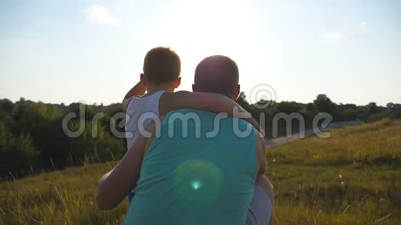 父亲和他的小儿子在日落时一起在户外度过爸爸和孩子坐在山上的绿草旁视频的预览图