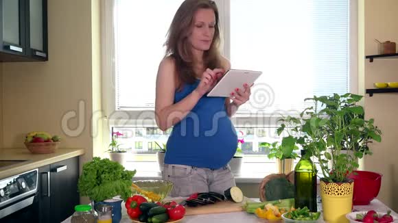 怀孕的家庭主妇拿着平板电脑上网搜索食谱视频的预览图