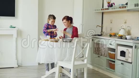 微笑的母亲和可爱的女儿一起做饼干用面团而坐在现代厨房在家里家庭视频的预览图