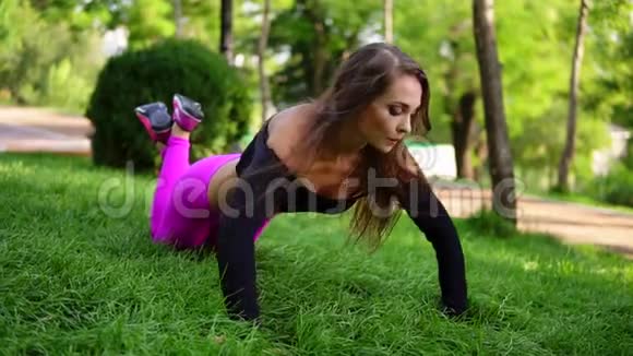 漂亮的黑发女人在公园的草地上做运动双膝俯卧撑慢镜头视频的预览图