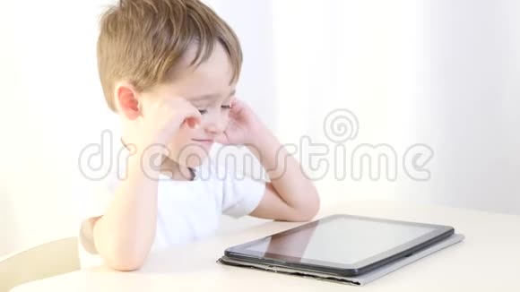 快乐的孩子坐在桌子旁玩平板电脑孩子乐于玩电子游戏儿童的概念视频的预览图