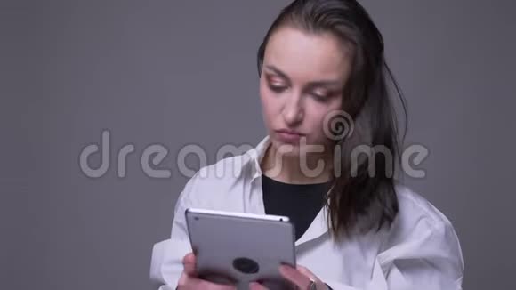 用平板电脑拍摄成年漂亮白人女性的特写照片并在灰色背景上隔离微笑视频的预览图