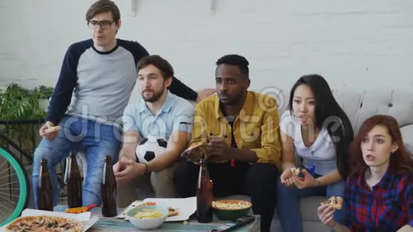 年轻朋友一起在家看电视上的足球赛对他们最喜欢的球队输球感到失望视频的预览图