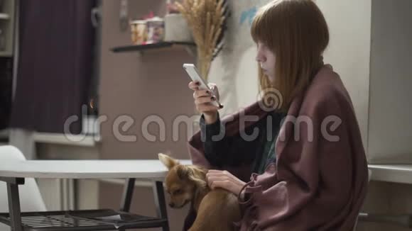 年轻漂亮的红发女人晚上在厨房用智能手机视频的预览图
