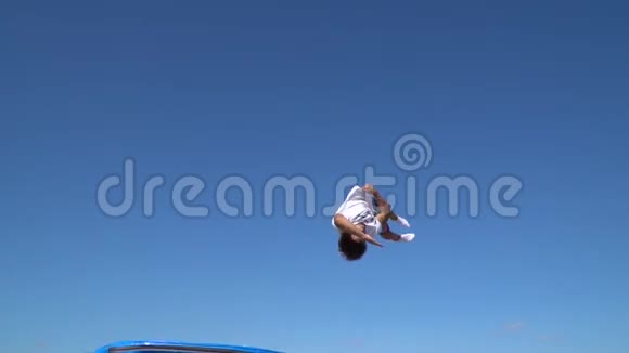 一个穿着短裤和T恤的成年男子跳得很高在蹦床上翻滚晴朗动作缓慢视频的预览图