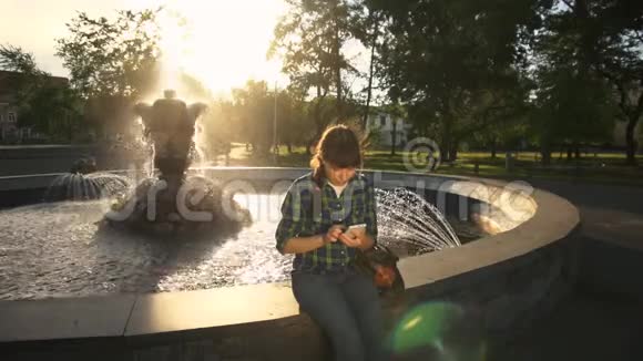 日落时分一位年轻女子在喷泉附近使用电话视频的预览图