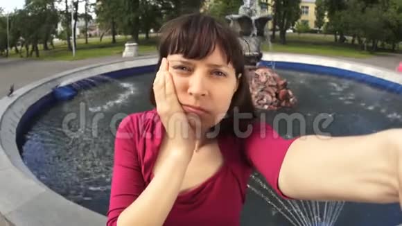 牙痛的年轻女子坐在公园的喷泉旁自拍视频的预览图