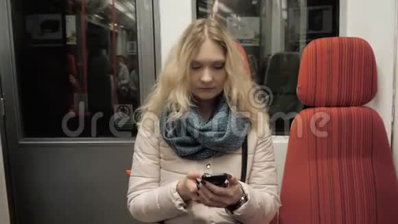地铁列车上年轻女性手机打字信息的画像金发女性智能手机视频的预览图