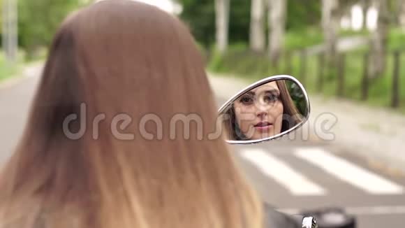 女孩画着她的嘴唇看着摩托车的镜子视频的预览图