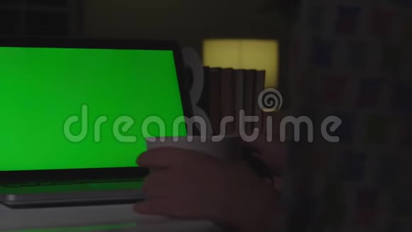 女人在家里用绿色屏幕在笔记本电脑上工作铬钥匙从后面看视频的预览图