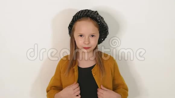 白色墙壁背景上戴着黑色闪亮帽子和连衣裙的小女孩的肖像视频的预览图