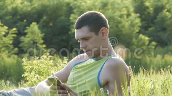 夏天年轻人坐在草地上在智能手机上打字视频的预览图