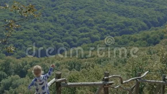 可爱的小男孩从森林的篱笆上挥手视频的预览图