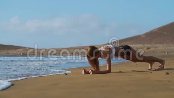 日落时美丽的运动女子在海滩上的木板位置的侧面景色视频的预览图