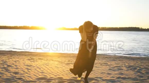 美丽的年轻女子在海滩上跳舞穿着黑色连衣裙在镜头前摆姿势视频的预览图