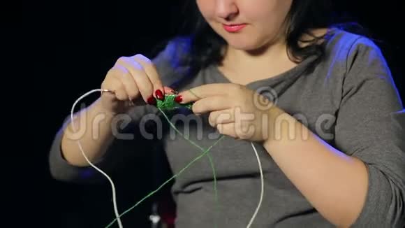 黑色背景的年轻女子在绿色线针上编织视频的预览图