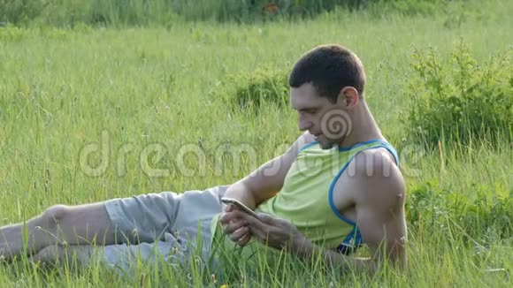 夏天年轻人坐在草地上在智能手机上打字视频的预览图