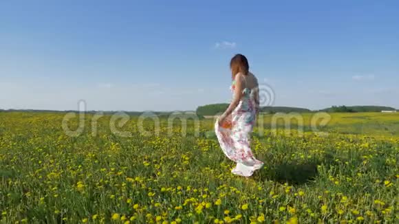 快乐的女人走在盛开的黄色田野上穿着一件随风飘扬的连衣裙视频的预览图
