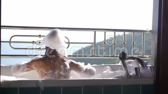 沐浴的年轻漂亮女人在热带度假胜地的泡沫浴缸中放松海景令人惊叹慢动作视频的预览图
