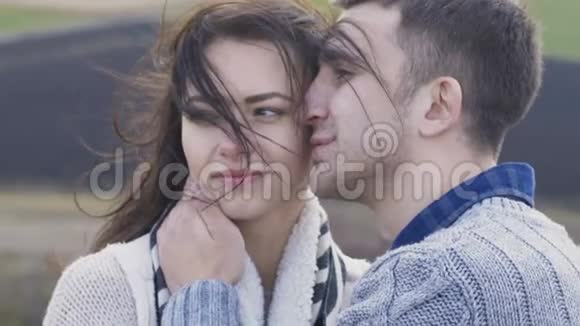 快乐的一对夫妇站在岩石上在刮风的日子里抚摸和亲吻视频的预览图