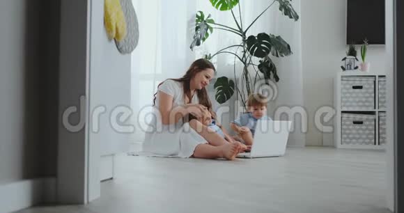 现代公寓妈妈和两个儿子坐在客厅的地板上看着笔记本电脑屏幕视频的预览图