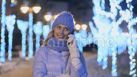 美丽的女孩穿着冬布在电话上交谈晚上灯光背景视频的预览图