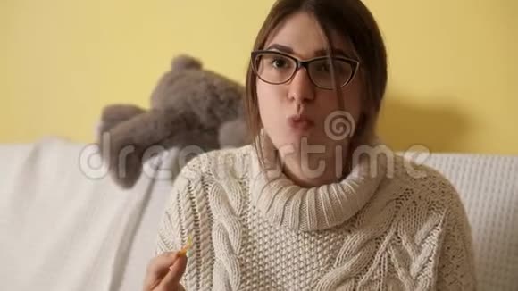 冬天晚上小女孩穿着白色毛衣在沙发上戴着眼镜看电视吃薯片视频的预览图