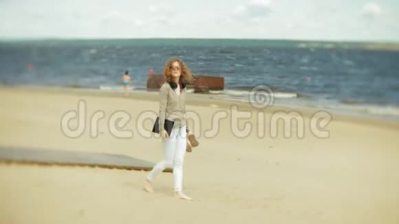 年轻的美女戴着耳机走在海滩上用平板电脑视频的预览图