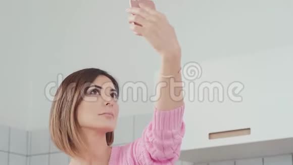 一个漂亮的女人拿着智能手机在厨房里自拍视频的预览图