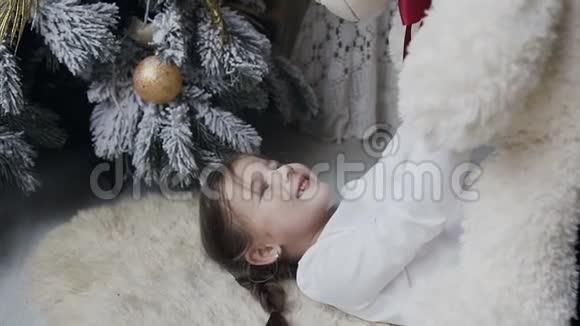 特写镜头迷人的女孩躺在柔软的白色地毯上和一只大毛绒熊玩寒假圣诞节视频的预览图