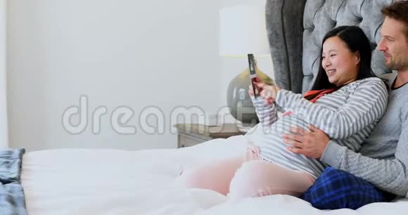 在卧室4k的男人和孕妇看超声波检查视频的预览图