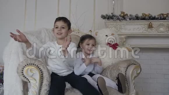 快乐的孩子一个男孩和一个女孩坐在一张大椅子上用金色的盒子抓住礼物圣诞节晚上视频的预览图