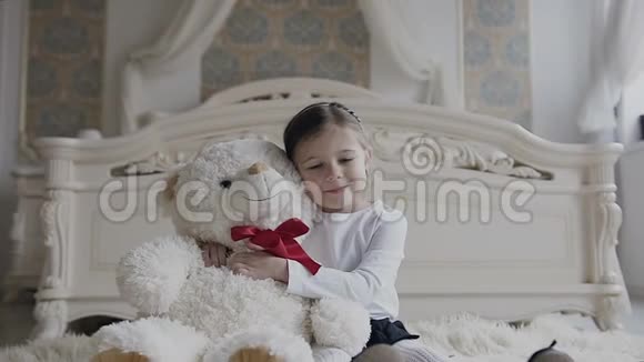 漂亮的小女孩坐在卧室的软地毯上带着一只大玩具软熊视频的预览图