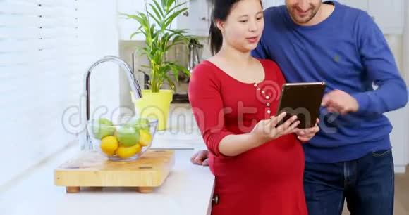 使用数码平板电脑的孕妇夫妇在家厨房4k视频的预览图