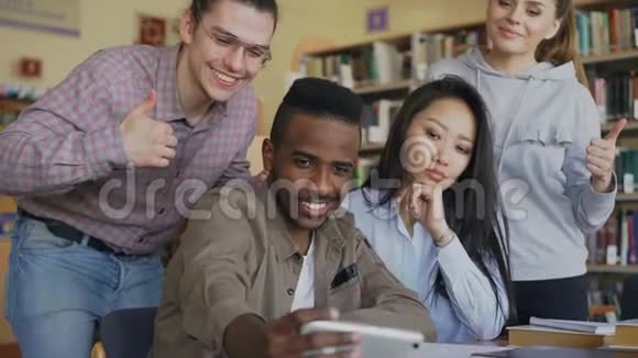 一群国际学生在大学图书馆的智能手机摄像头上开心地微笑和自拍视频的预览图