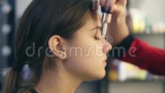 化妆师在一个年轻女孩的脸上涂上遮瑕膏完美妆容的基础慢镜头视频的预览图