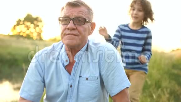 一个卷曲的孙子求助于他的祖父并从后面拥抱他祖父告诉男孩一些事笑了视频的预览图