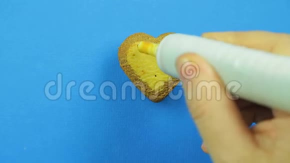 女性的手在蓝色背景的心形饼干上画有趣的表情符号上面有棕色的糖霜视频的预览图