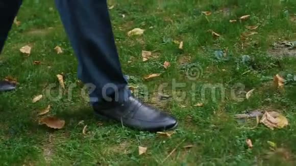 穿着蓝色西装和时髦的黑色鞋子在草地上行走的无名男子视频的预览图