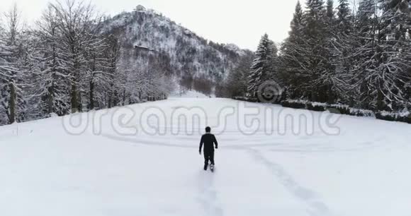 空中向前飞人穿着雪鞋走在山上白雪覆盖的田野在寒冷的冬天松林森林附近视频的预览图