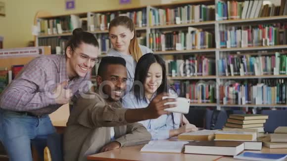 一群国际学生在大学图书馆的智能手机摄像头上开心地微笑和自拍视频的预览图