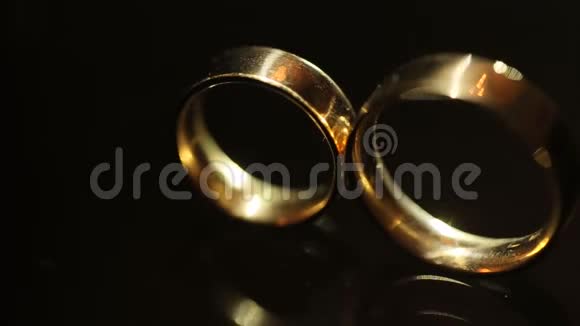 在黑暗的背景上近距离观看金色的结婚戒指一束束光照亮了环视频的预览图
