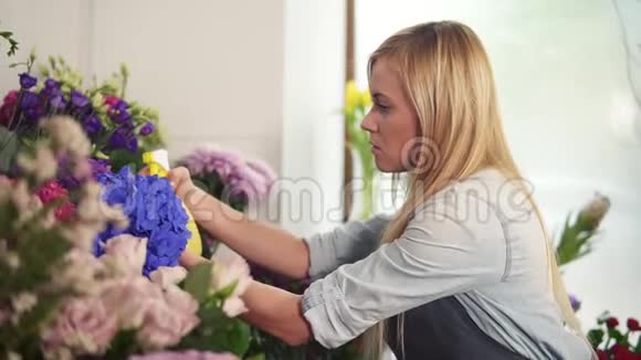 年轻迷人的金发女性花店在花束上喷水慢镜头视频的预览图