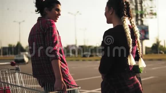 镜头转悠两个迷人的时尚女孩站在购物车边停车在日落时交谈视频的预览图