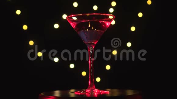 明亮的红色鸡尾酒在玻璃旋转在黑暗的背景与模糊的光视频的预览图