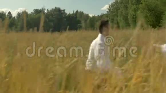 一个年轻的女人和一个穿着白色西装的男人逃跑见面拥抱在阳光明媚的日子里在一片麦田里视频的预览图